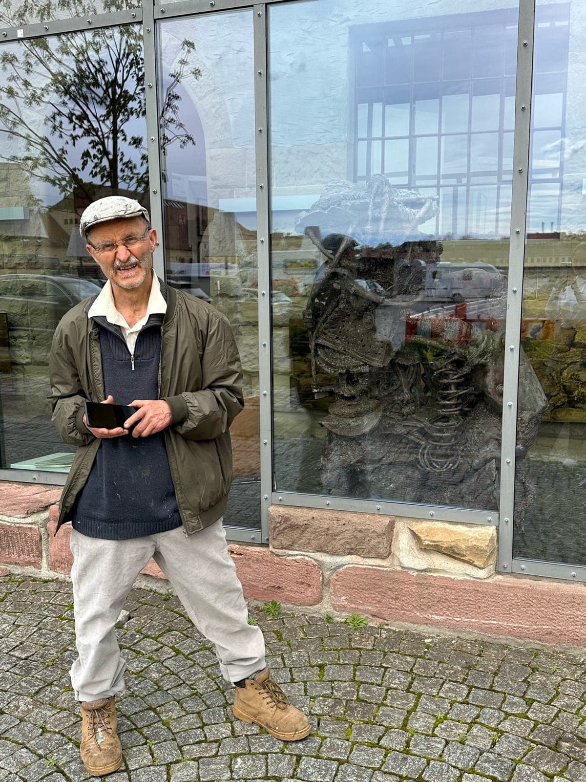 Gerd Georg Hirschmann steht vor einem Schaufenster, hinter der Scheibe eine seiner Metallskulpturen.